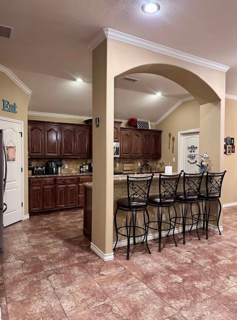 3113 San Pedro Dr, Odessa, TX 79765 - kitchen with a kitchen breakfast bar, arched walkways, ornamental molding, decorative backsplash, and dark brown cabinetry