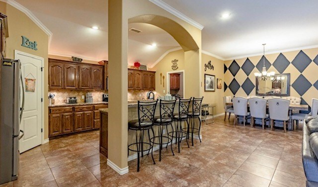 3113 San Pedro Dr, Odessa, TX 79765 - kitchen featuring freestanding refrigerator, a kitchen breakfast bar, crown molding, arched walkways, and a chandelier