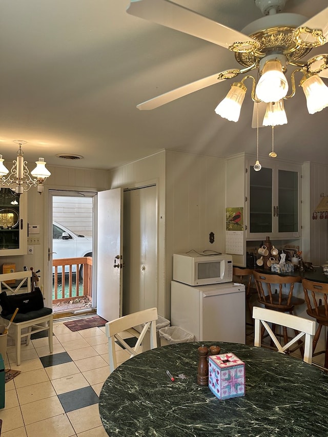 tiled dining space featuring ceiling fan with notable chandelier