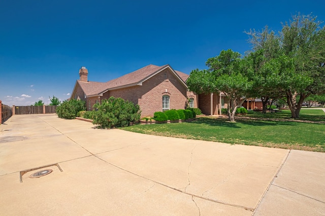 view of side of home with fence, a chimney, a lawn, and brick siding