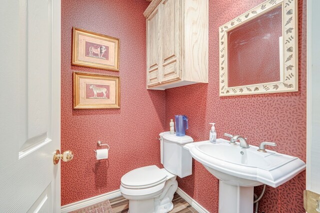 half bathroom with toilet, wallpapered walls, and wood finished floors