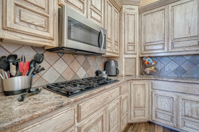 kitchen featuring backsplash, stainless steel microwave, cream cabinetry, and gas stovetop