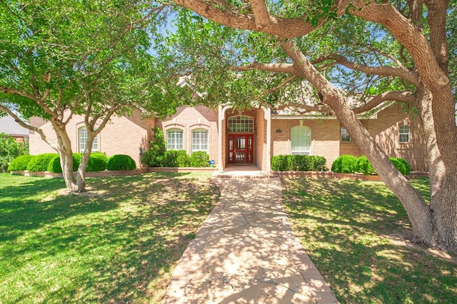 view of property hidden behind natural elements with a front lawn and brick siding
