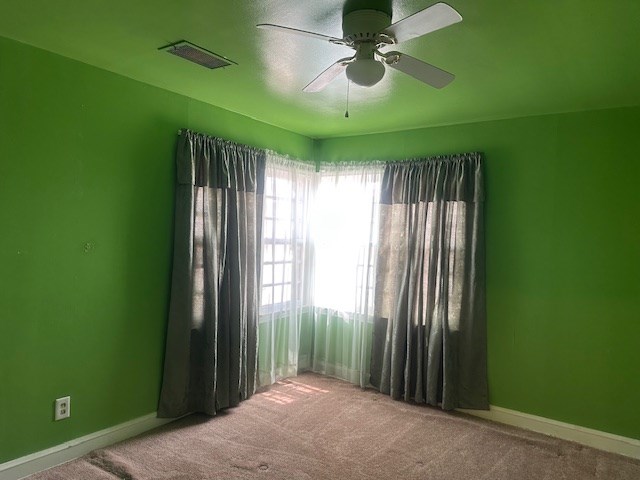 carpeted spare room with a ceiling fan and baseboards