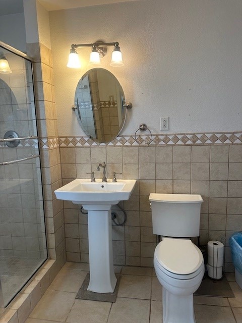 full bath featuring tile walls, a shower stall, a wainscoted wall, toilet, and tile patterned floors