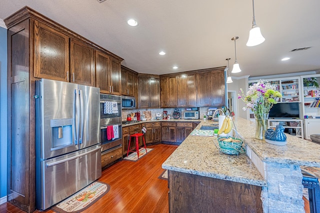 kitchen featuring stainless steel appliances, wood finished floors, backsplash, light stone countertops, and a sink