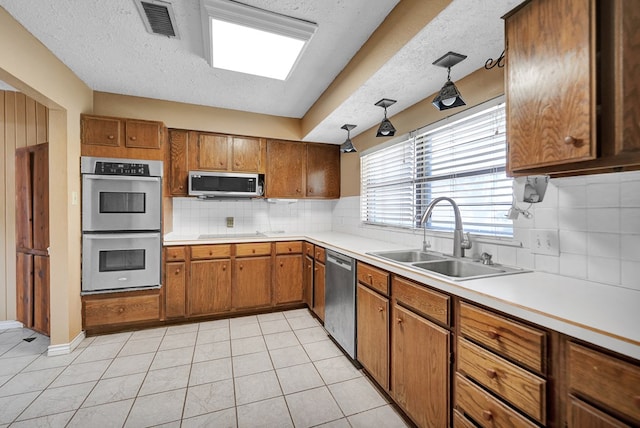 4205 Irvin Dr, Midland, TX 79705 - kitchen with stainless steel appliances, a sink, brown cabinets, tasteful backsplash, and a textured ceiling