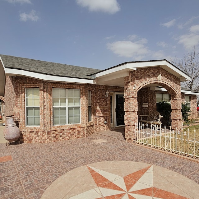 view of front of property with roof with shingles, a patio, and brick siding