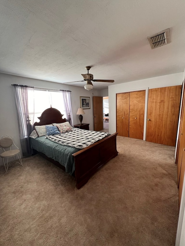 bedroom featuring a textured ceiling, carpet floors, ceiling fan, and multiple closets