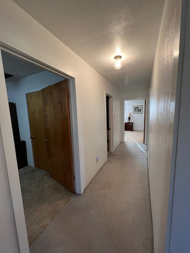 corridor featuring light colored carpet and a textured ceiling