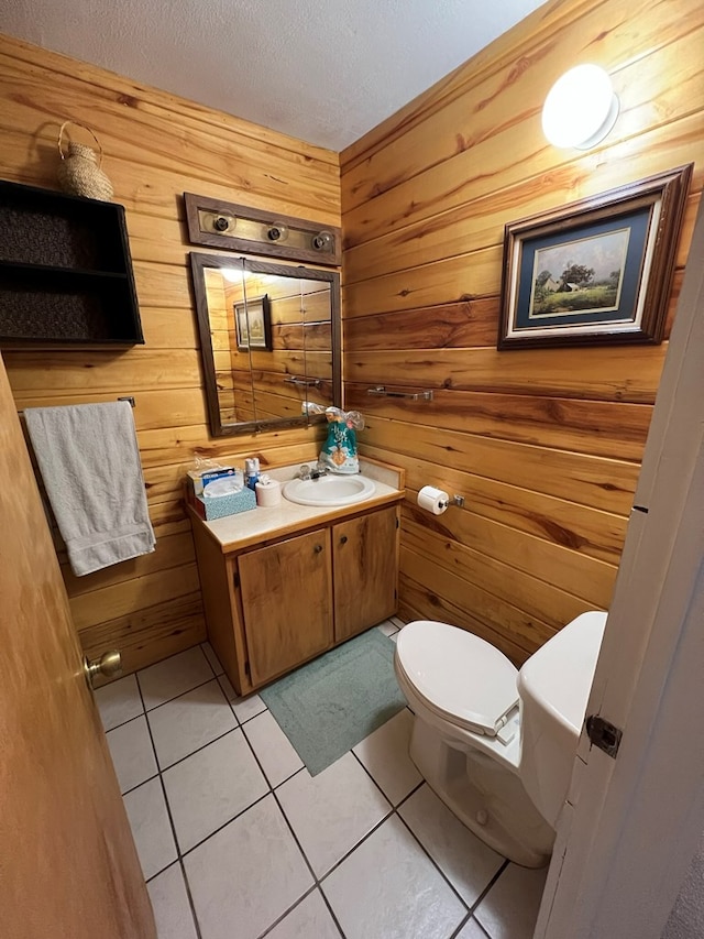 bathroom featuring vanity, tile patterned floors, wooden walls, toilet, and a textured ceiling