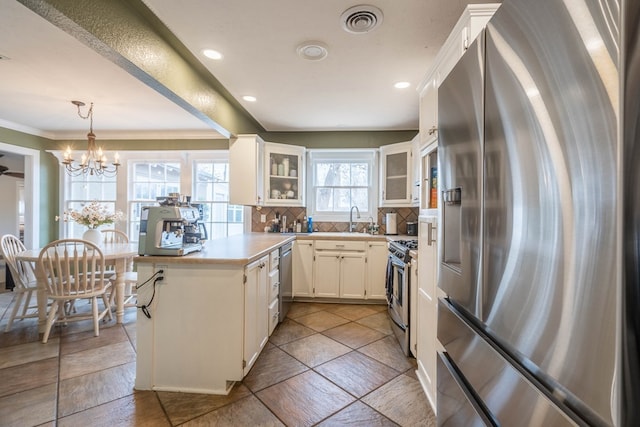 kitchen with stainless steel appliances, tasteful backsplash, a chandelier, glass insert cabinets, and a peninsula