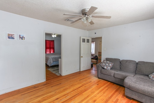 living room featuring ceiling fan, a textured ceiling, visible vents, baseboards, and light wood-style flooring