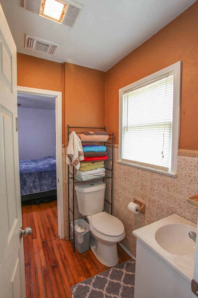 half bath with visible vents, wood finished floors, toilet, and tile walls