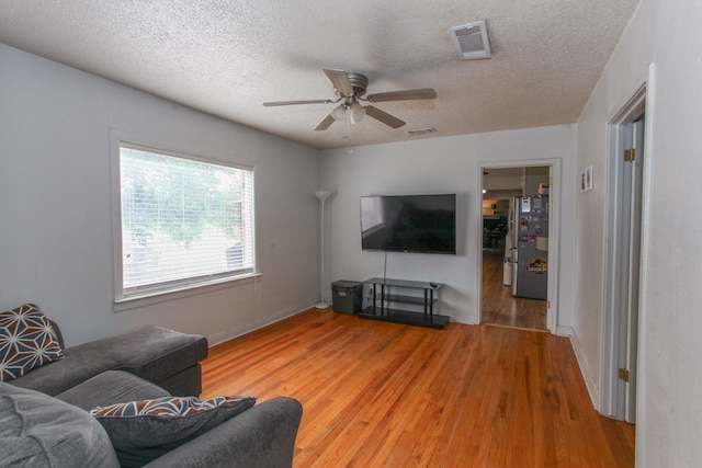 living area with a ceiling fan, light wood finished floors, a textured ceiling, and visible vents