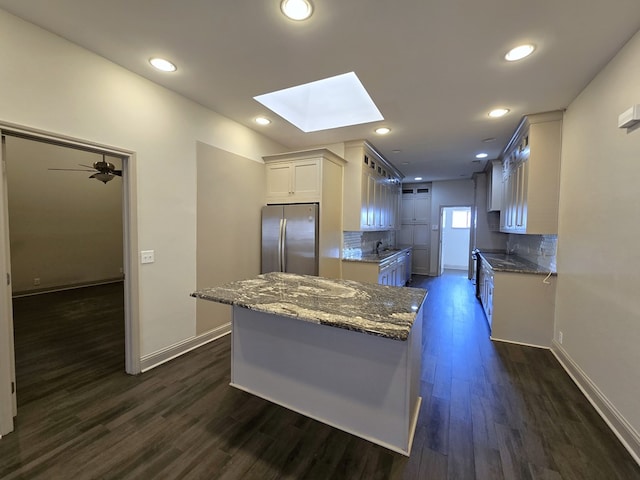 kitchen with a skylight, white cabinets, backsplash, freestanding refrigerator, and dark stone counters