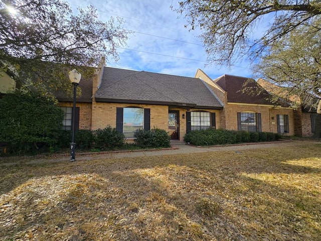 view of front of property with brick siding, roof with shingles, and a front yard