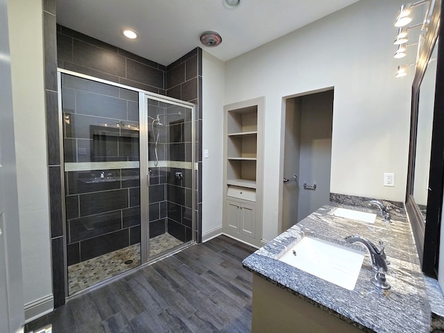 bathroom with double vanity, a shower stall, a sink, and wood finished floors