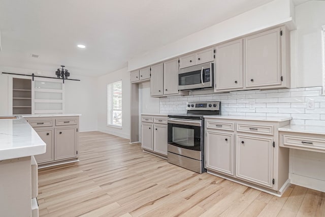 1017 Ward St, Midland, TX 79701 - kitchen featuring stainless steel appliances, light wood-type flooring, decorative backsplash, a barn door, and recessed lighting