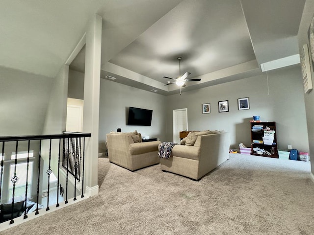 carpeted living area with a tray ceiling, visible vents, ceiling fan, and attic access