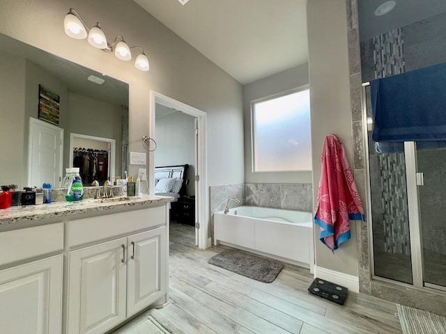 bathroom with vanity, wood finished floors, a bath, vaulted ceiling, and a tile shower