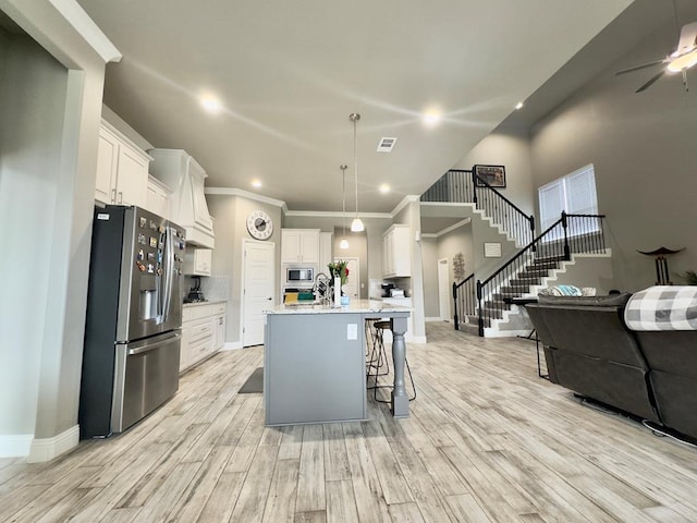 kitchen featuring light countertops, open floor plan, ornamental molding, stainless steel appliances, and light wood-style flooring