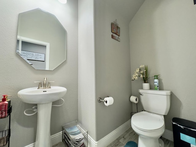 half bathroom featuring toilet, baseboards, and a sink