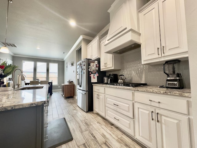 kitchen featuring decorative backsplash, crown molding, appliances with stainless steel finishes, a sink, and custom range hood