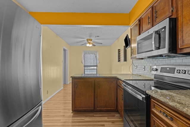 kitchen featuring light hardwood / wood-style flooring, appliances with stainless steel finishes, a textured ceiling, decorative backsplash, and kitchen peninsula