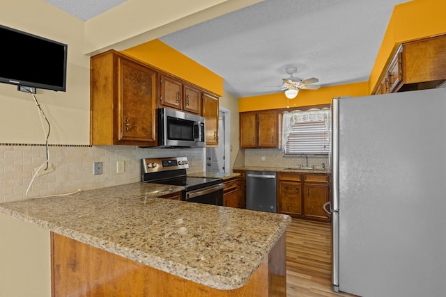 kitchen featuring appliances with stainless steel finishes, tasteful backsplash, light stone countertops, kitchen peninsula, and light wood-type flooring