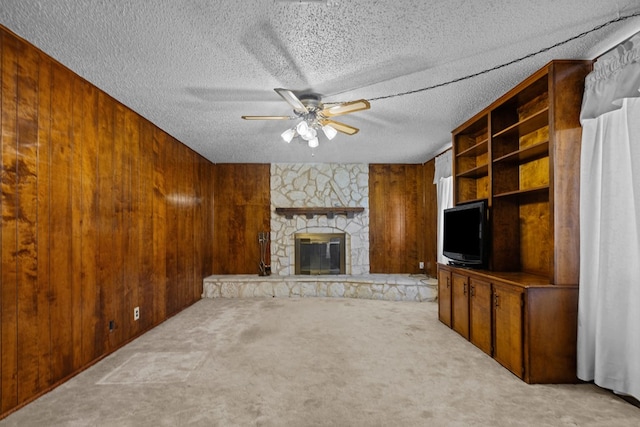 unfurnished living room with a stone fireplace, wood walls, a textured ceiling, light carpet, and ceiling fan