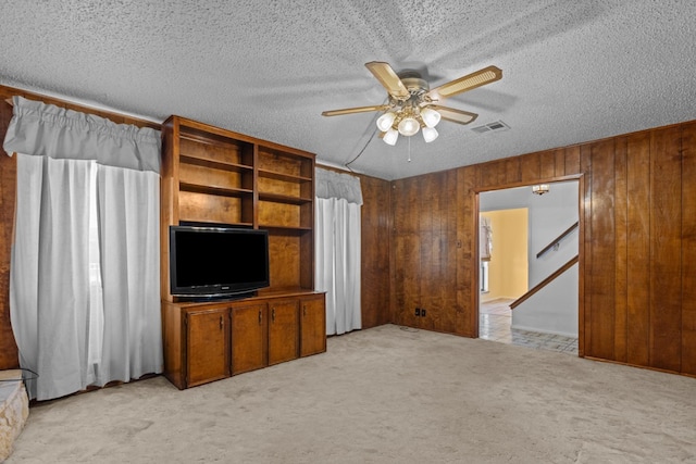 unfurnished living room with ceiling fan, light carpet, a textured ceiling, and wooden walls