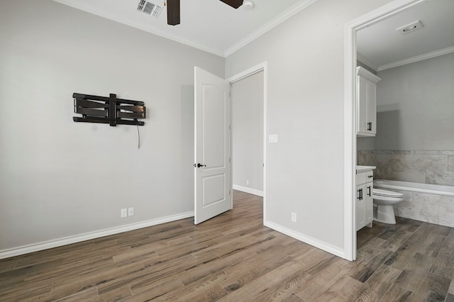 unfurnished bedroom featuring wood finished floors, ornamental molding, ensuite bathroom, baseboards, and ceiling fan