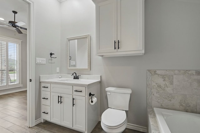 full bathroom featuring a ceiling fan, baseboards, vanity, tiled tub, and toilet