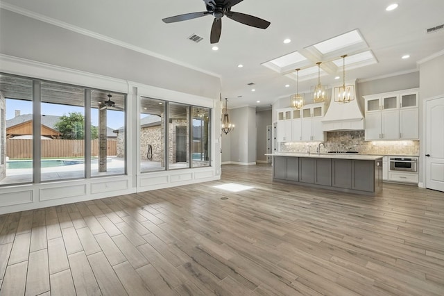 kitchen with a ceiling fan, custom range hood, ornamental molding, decorative backsplash, and a chandelier