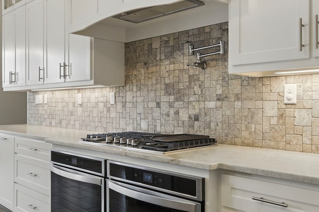 kitchen with appliances with stainless steel finishes, decorative backsplash, white cabinets, under cabinet range hood, and light stone counters