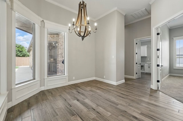 unfurnished dining area featuring a chandelier, wood finished floors, ornamental molding, and baseboards