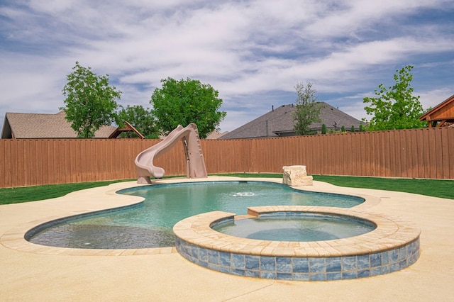 view of swimming pool featuring a water slide, a fenced backyard, and a pool with connected hot tub