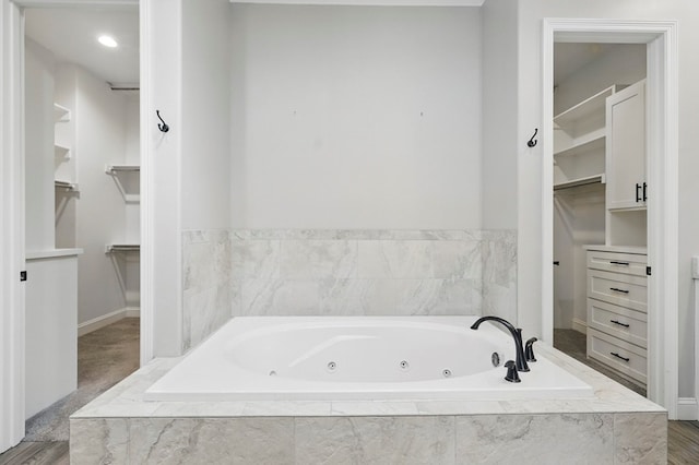 full bath with a walk in closet, a tub with jets, and baseboards