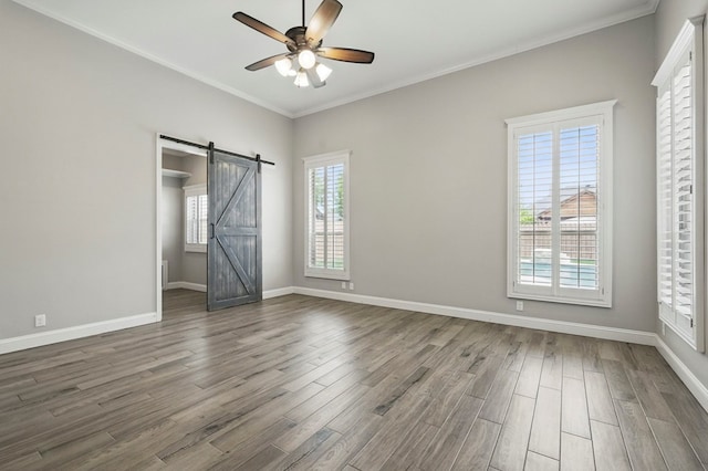 unfurnished bedroom with a barn door, wood finished floors, baseboards, ornamental molding, and a ceiling fan