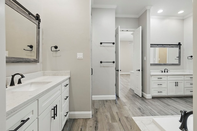 bathroom featuring ornamental molding, baseboards, two vanities, wood finished floors, and recessed lighting