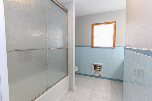 2004 State St, Big Spring, TX 79720 - full bathroom with heating unit, tile walls, shower / bath combination with glass door, wainscoting, and tile patterned flooring