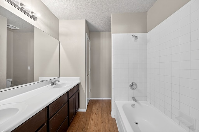 3237 Preston Dr, Midland, TX 79707 - bathroom featuring wood finished floors, double vanity, washtub / shower combination, and a textured ceiling