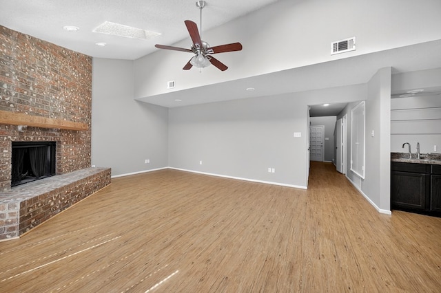 3237 Preston Dr, Midland, TX 79707 - unfurnished living room with a brick fireplace, a ceiling fan, light wood finished floors, high vaulted ceiling, and bar with sink