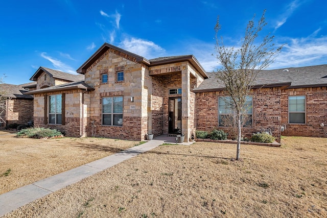 view of front of home featuring a front yard, brick siding, and stone siding