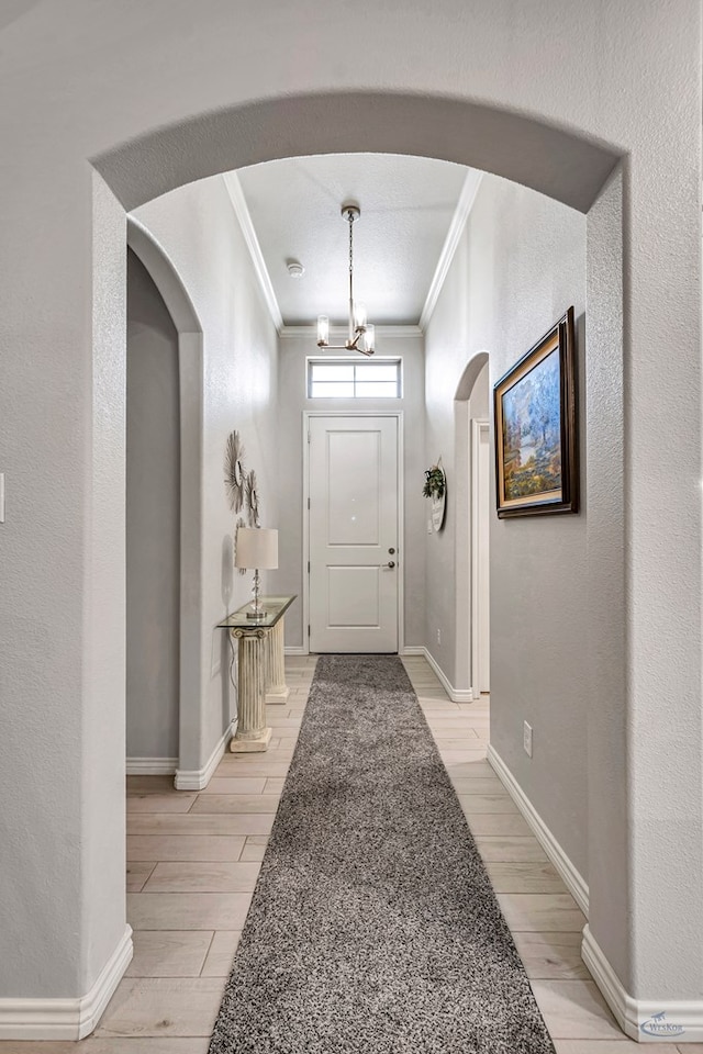 entryway featuring wood finish floors, ornamental molding, arched walkways, baseboards, and a chandelier