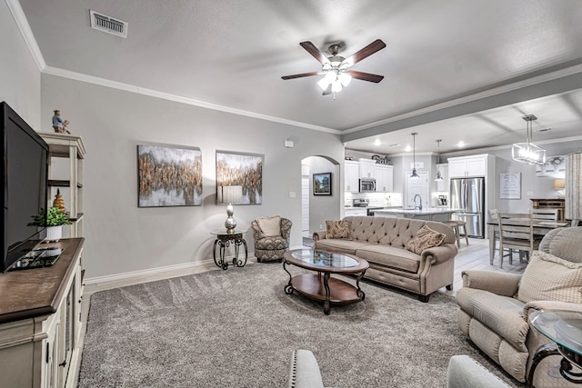 living area with visible vents, baseboards, ornamental molding, light carpet, and arched walkways