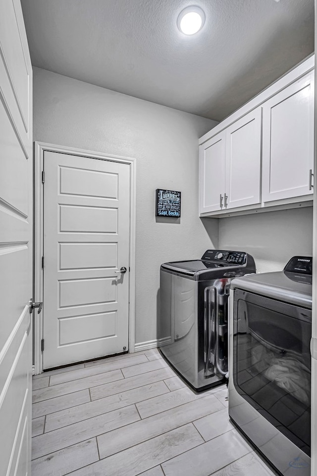 washroom with baseboards, wood finish floors, cabinet space, a textured ceiling, and washing machine and dryer