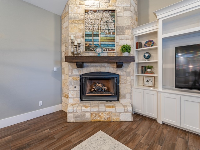 unfurnished living room with dark wood-style floors, baseboards, and a stone fireplace
