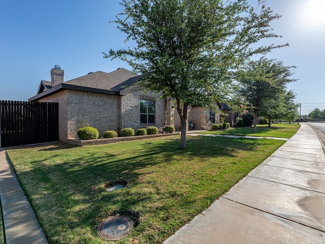 view of property exterior featuring a lawn, a chimney, brick siding, and fence